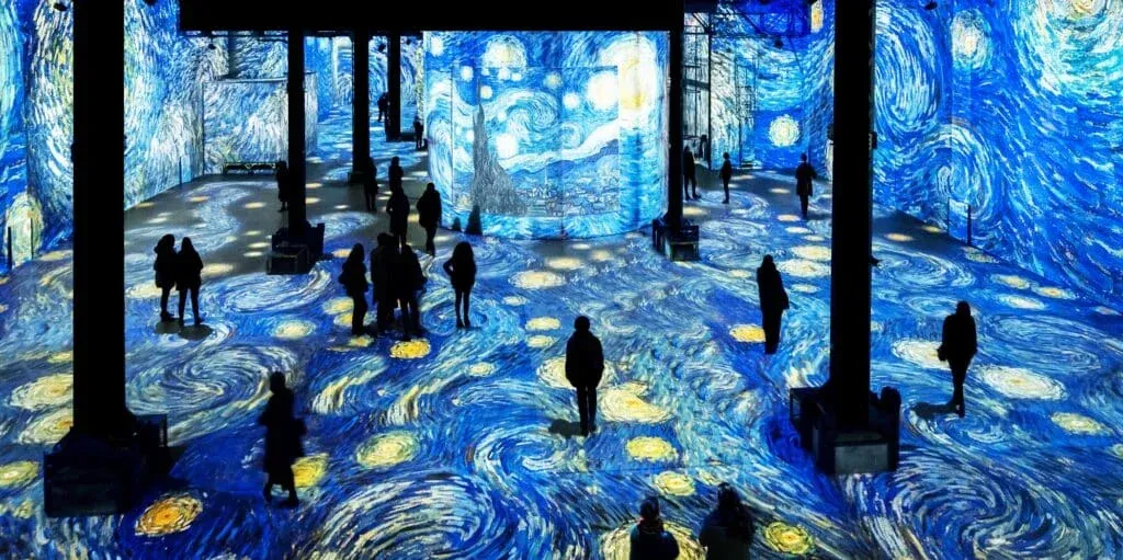 People walking through an immersive exhibit featuring projections of Van Gogh's Starry Night across the floor and walls.