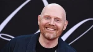 A bald man with a red beard smiling in front of a black background with white lines.