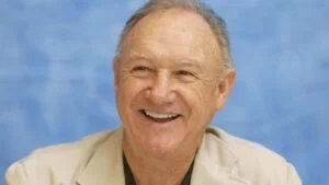 A smiling elderly man wearing a light-colored suit with a blue background.