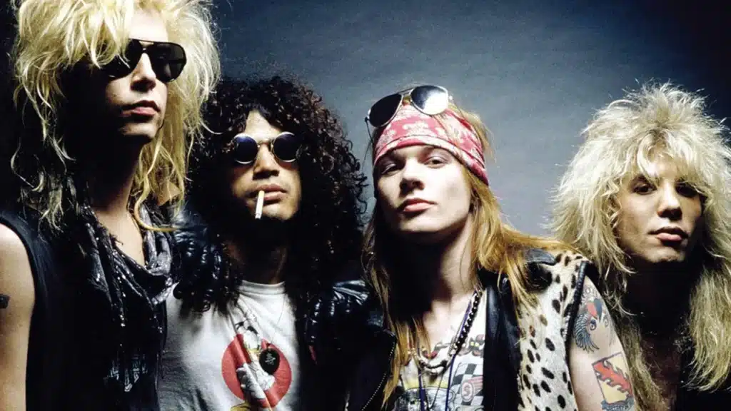 Four men wearing rock band attire including sunglasses, bandanas, and leather, posing against a plain background.