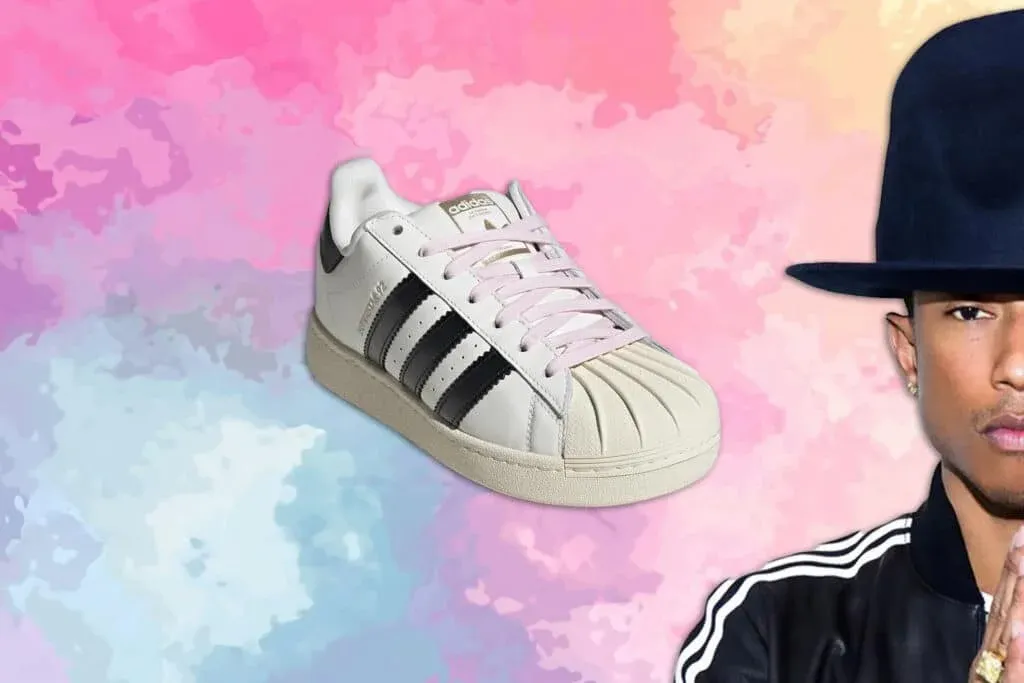 A white adidas sneaker with black stripes and light laces is displayed against a colorful watercolor background. Partially visible on the right is a person wearing a large hat and a black jacket with white stripes.