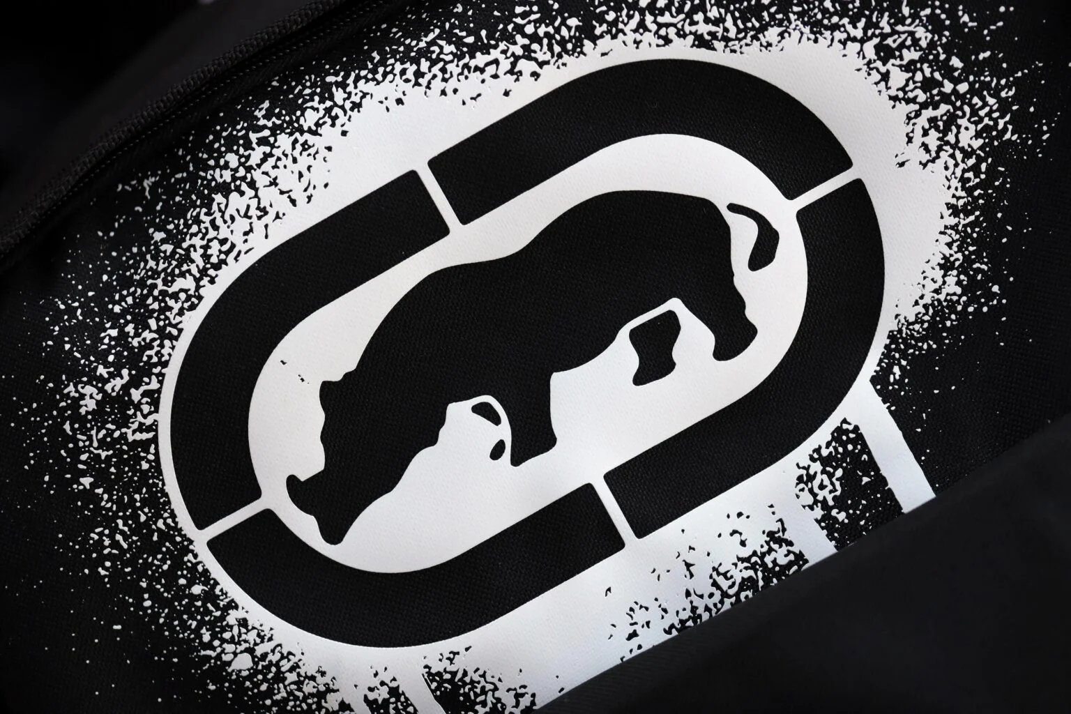A black and white image showing the silhouette of a rhinoceros inside an oval shape, with a speckled texture surrounding it.