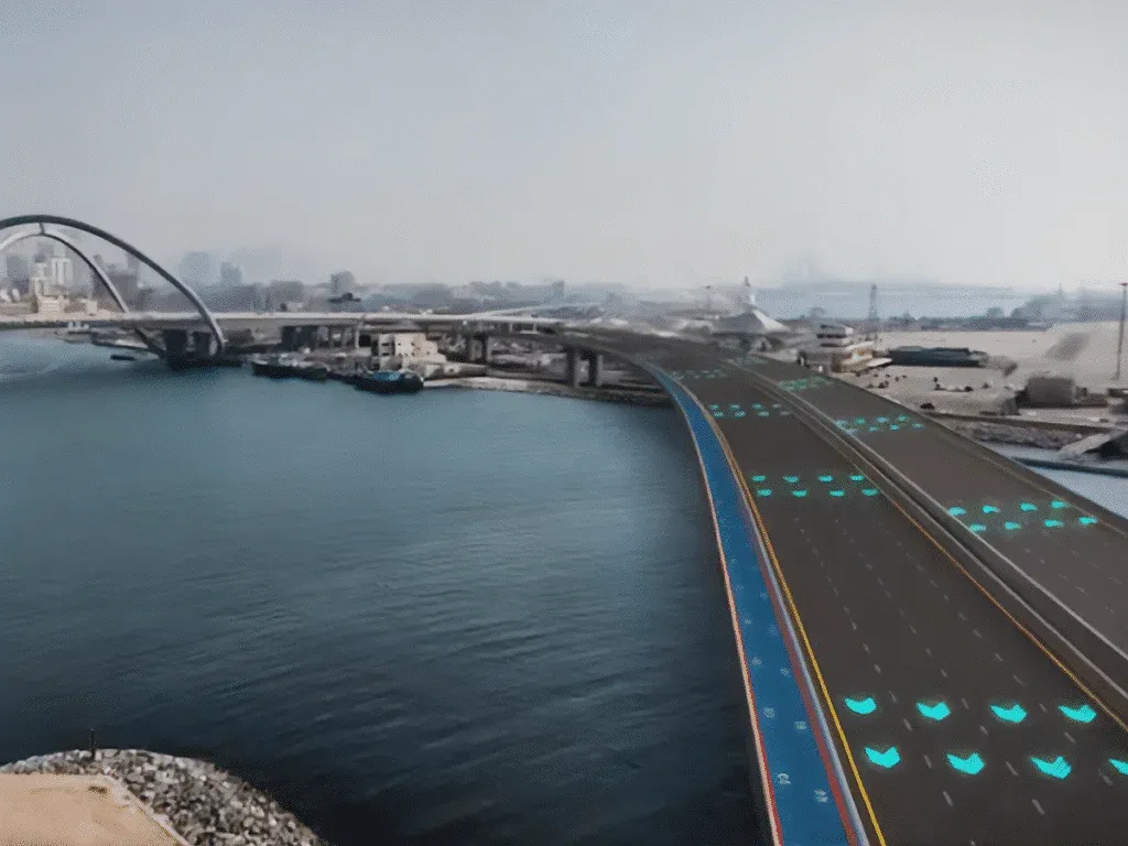 A futuristic bridge over a body of water with illuminated patterns on the road surface, leading into a cityscape with buildings in the background.