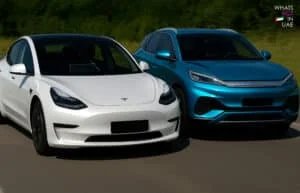 A white car next to a blue SUV driving on a road, with a green forest in the background and text "Whats Hot in UAE" at the top right corner.