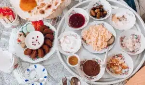 A breakfast spread with various dishes on decorative floral plates, including falafel, fresh vegetables, various dips, olives, scrambled eggs, and bread on a tray.