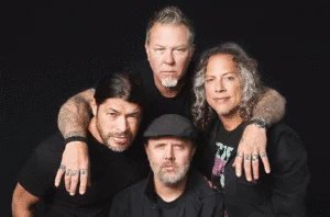 Four men pose together against a black background, with two in front and two standing behind, all wearing dark clothing and displaying serious expressions.