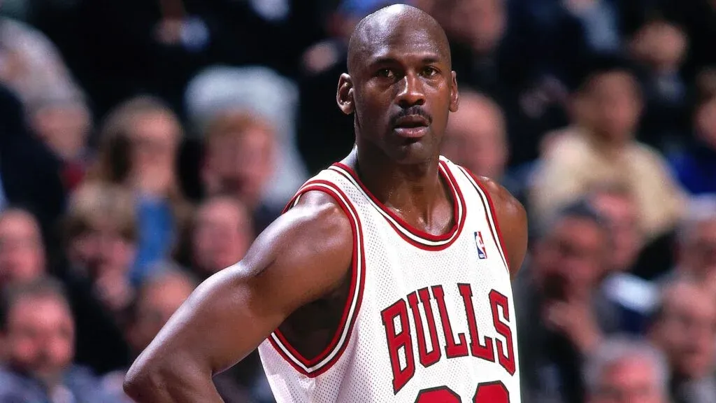 A basketball player wearing a white Bulls jersey stands on a court, appearing focused during a game.