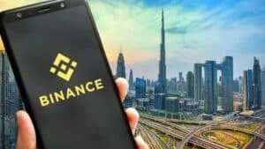 A smartphone displaying the Binance logo is held up against the backdrop of a modern cityscape, including the Burj Khalifa in Dubai.