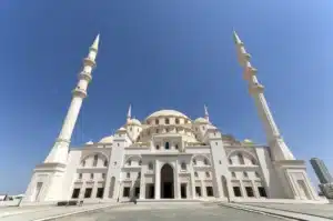 A grand white mosque featuring a large central dome and four tall minarets, set against a clear blue sky.