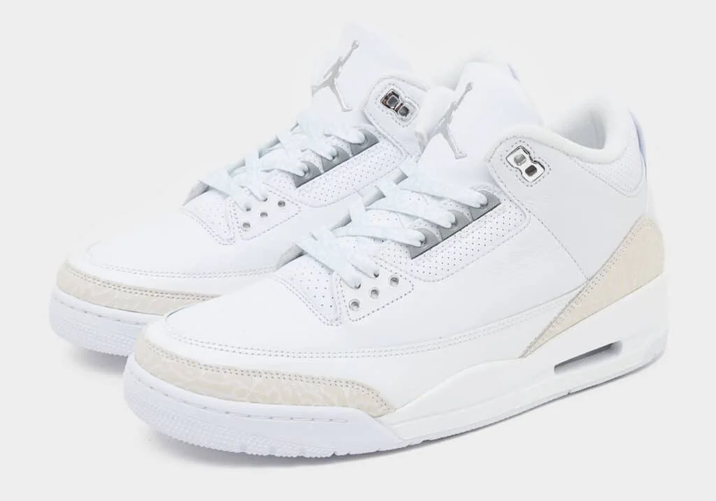 A pair of white sneakers featuring a sleek design with textured detailing, a perforated leather upper, and a visible air cushioning system in the sole.