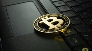 A gold Bitcoin coin resting on a black laptop keyboard, highlighting the cryptocurrency theme in a tech environment.