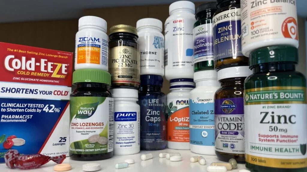 A collection of various zinc supplements and cold remedies, including Cold-Eze, Zicam, and Nature's Way, displayed together with different bottles and boxes, showcasing their labels and packaging. Several pills are scattered on the surface in front of the products.