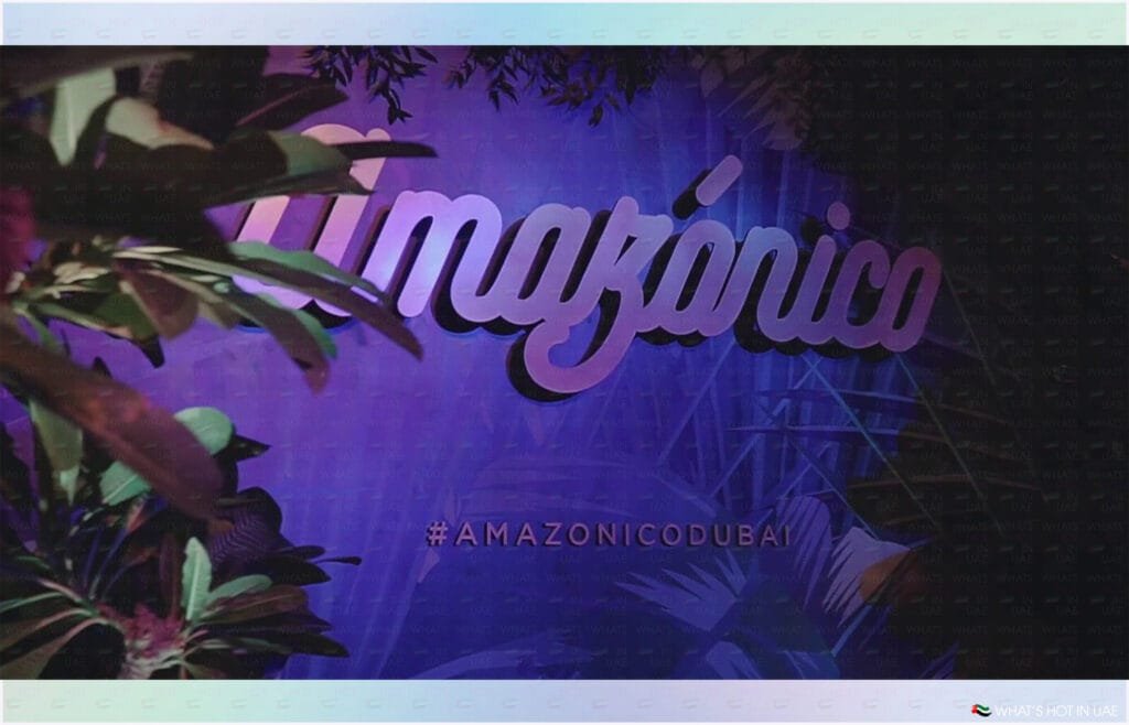 A vibrant sign displaying the word 'Amazónico' lit in purple and pink, surrounded by tropical foliage with the hashtag '#AMAZONICODUBAI' visible below.