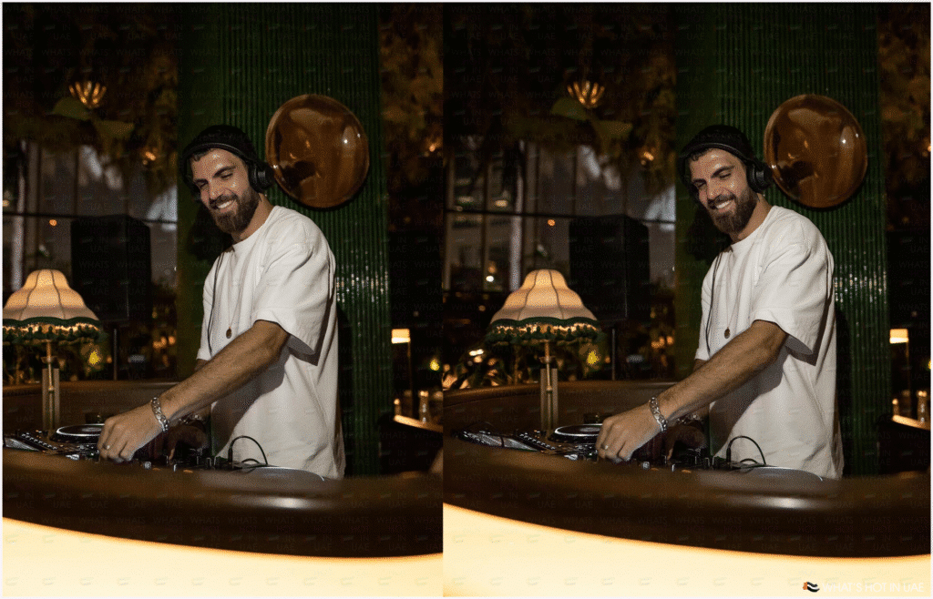 A DJ wearing headphones and a white T-shirt is smiling while mixing music at a DJ booth in a dimly lit room with green decor and vintage lampshades.