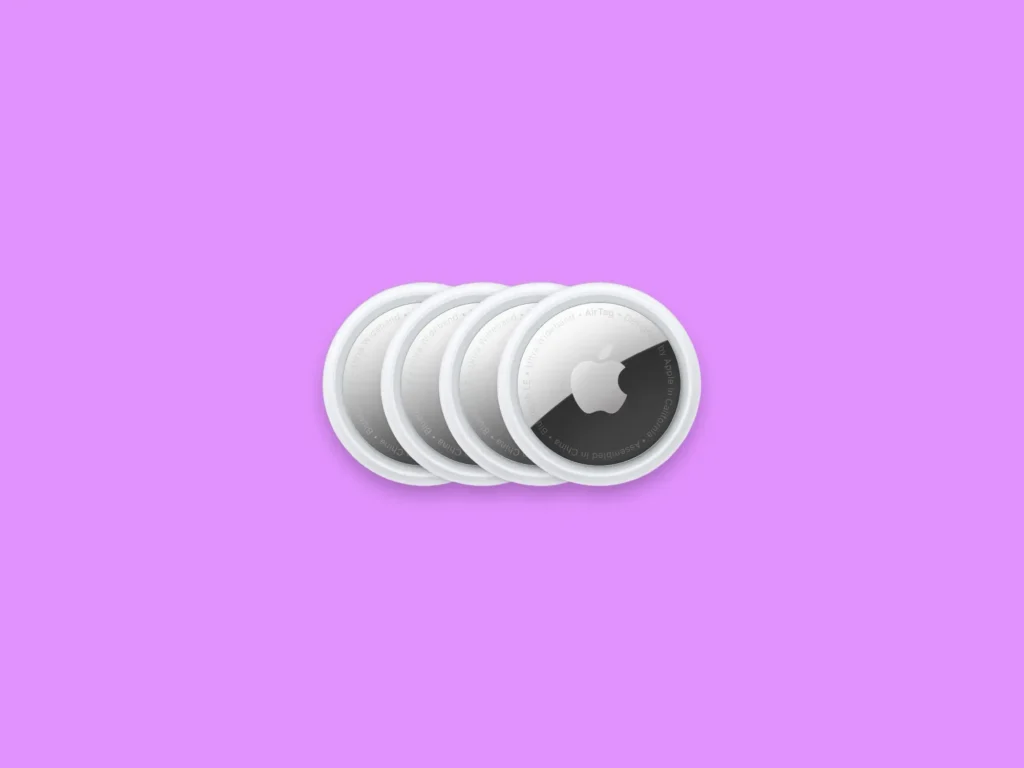 Four white Apple AirTags arranged in a row on a purple background.