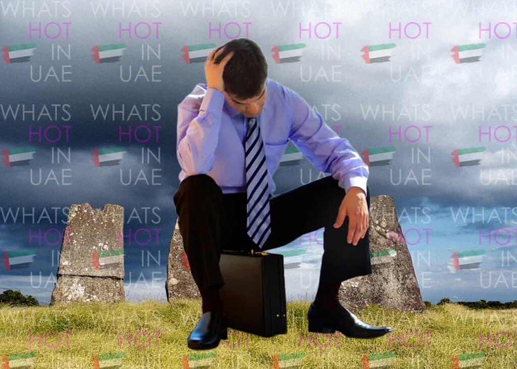 A man in a suit crouching with a briefcase, appearing distressed, set against a surreal background featuring stones and the repeated text