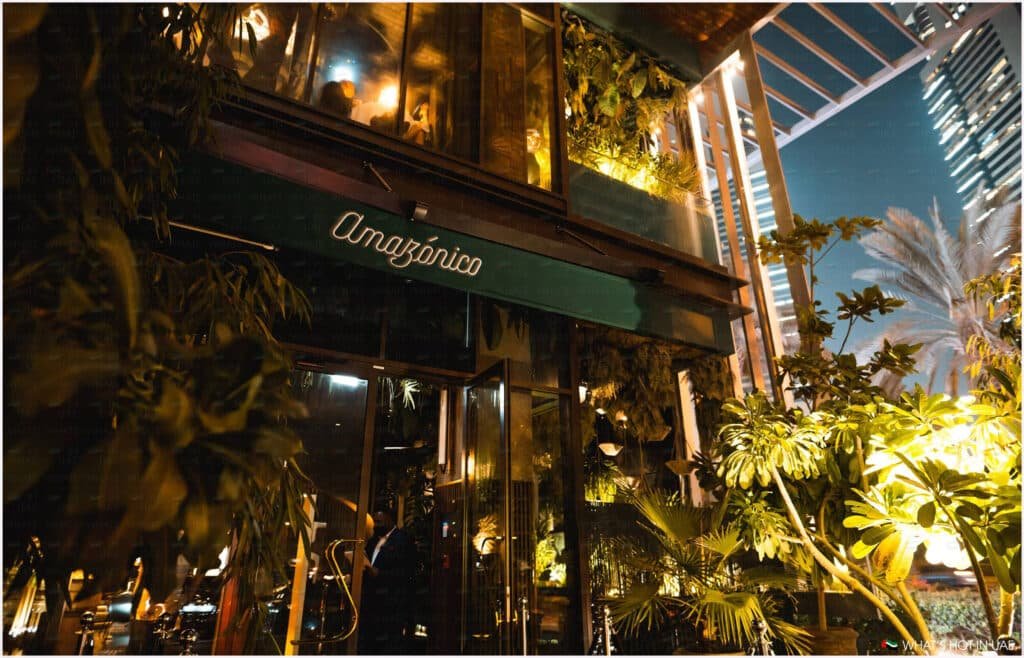 Outdoor view of a tropical-themed restaurant named 'Amazonico' at night, with lush greenery and warm lighting, displaying a lively ambiance.