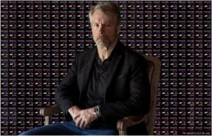 A man with gray hair and a beard is seated wearing a black jacket and a watch, against a backdrop featuring the repeated text "WHAT'S HOT IN UAE" and the UAE flag.