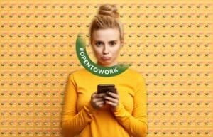 A person with a bun hairstyle wears a yellow long-sleeve shirt and holds a smartphone, standing in front of a backdrop with repeated patterns of UAE flags and text saying, "WHAT'S HOT IN UAE." A circular graphic with the hashtag "#OPENTOWORK" is overlaid on the image.