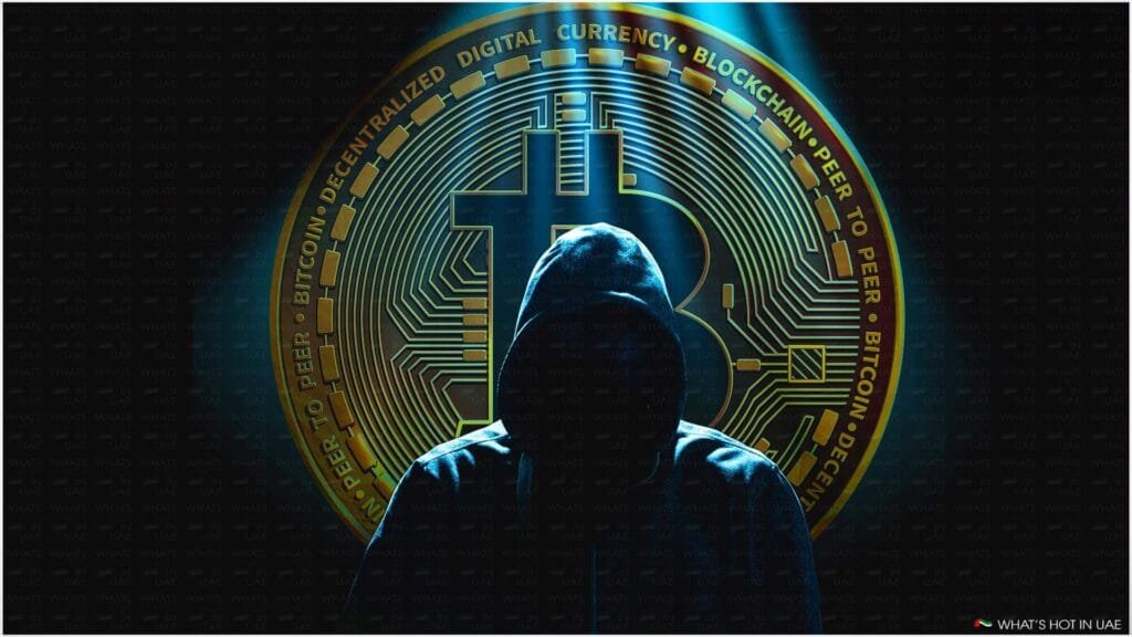 A hooded figure is silhouetted against the background of a large Bitcoin symbol and circuitry, suggestive of digital currency themes.