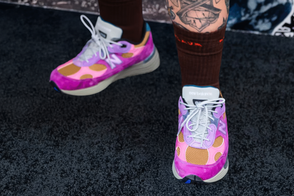 A pair of colorful sneakers with a pink, purple, and orange design, worn with brown socks and visible tattoos on the legs.