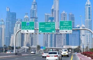 A busy highway in Dubai with road signs overhead directing towards Sheikh Zayed Road, Al Naseem Street, and Al Rabeea Street, with a backdrop of modern skyscrapers and clear blue sky.