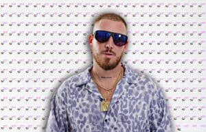 A man wearing sunglasses, a leopard-print shirt, and layered gold necklaces stands in front of a backdrop featuring the words 'WHAT'S HOT IN UAE' along with small UAE flags. Hugel Live at Pure Pacha