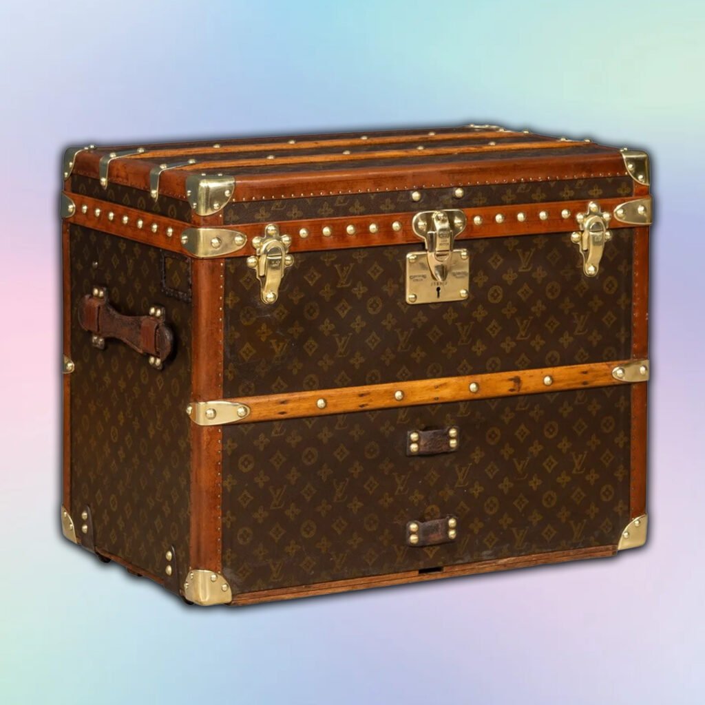 A vintage steamer trunk with dark brown leather and a monogram pattern, featuring wooden trim and metal hardware, including latches and corner protectors.