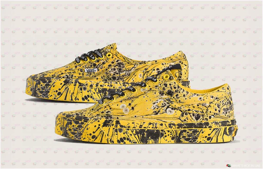 Yellow SR Studio Vans sneakers with a black splattered paint design and text on the laces, displayed against a patterned background.
