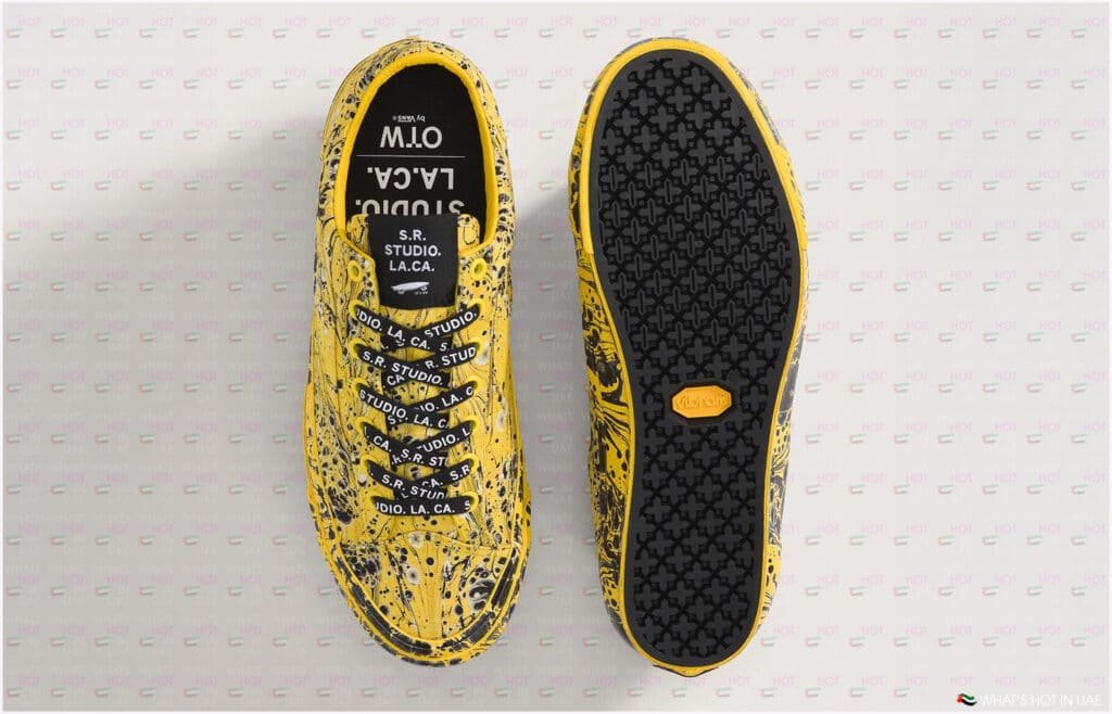 A pair of yellow SR Studio sneakers with a black splatter pattern, featuring customized laces and tags displaying 'S.R. Studio. L.A. C.A.' branding, shown from the top view and sole view, with a Vibram sole.