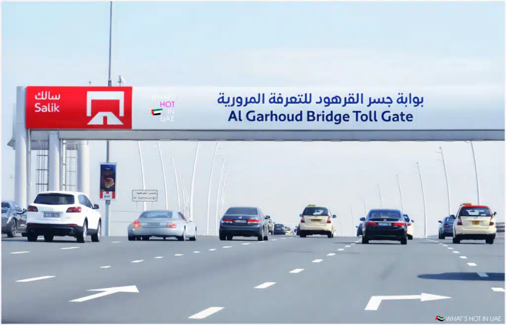 Cars driving on a highway underneath the Al Garhoud Bridge Toll Gate in UAE, with a sign displaying 'Salik' and Arabic text.