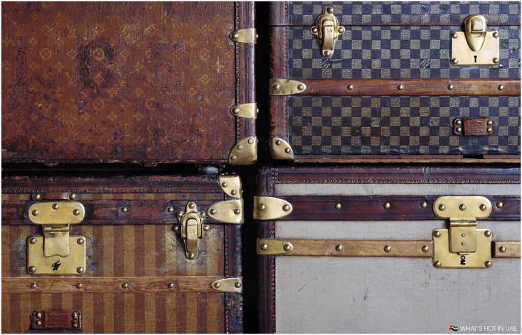 Close-up of a stack of vintage trunks with brass hardware, featuring various textures and patterns, including striped and checkered designs.