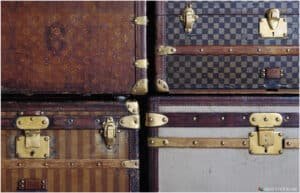 Close-up of a stack of vintage trunks with brass hardware, featuring various textures and patterns, including striped and checkered designs.