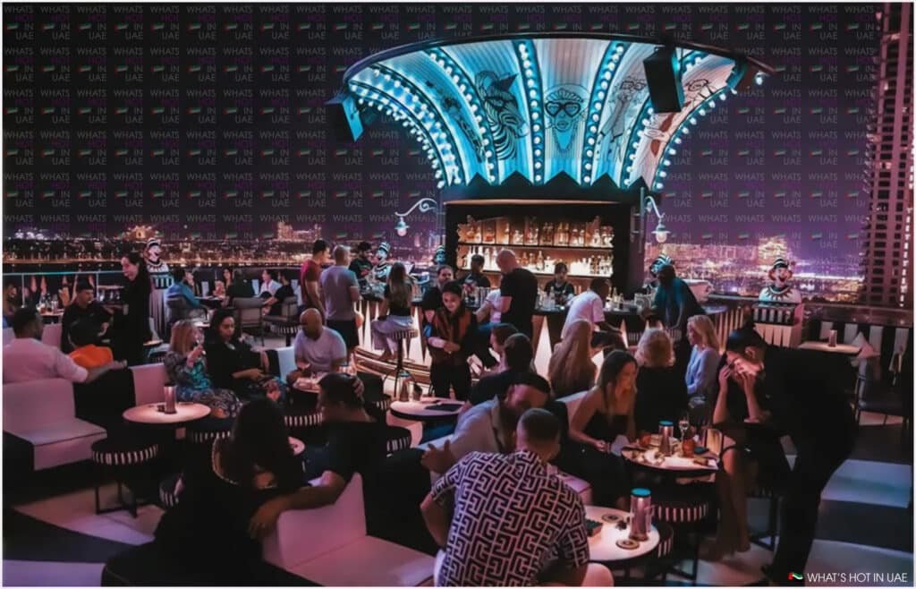 A lively bar scene with people socializing and sitting at tables under a decorative illuminated ceiling, showcasing an urban skyline backdrop.
