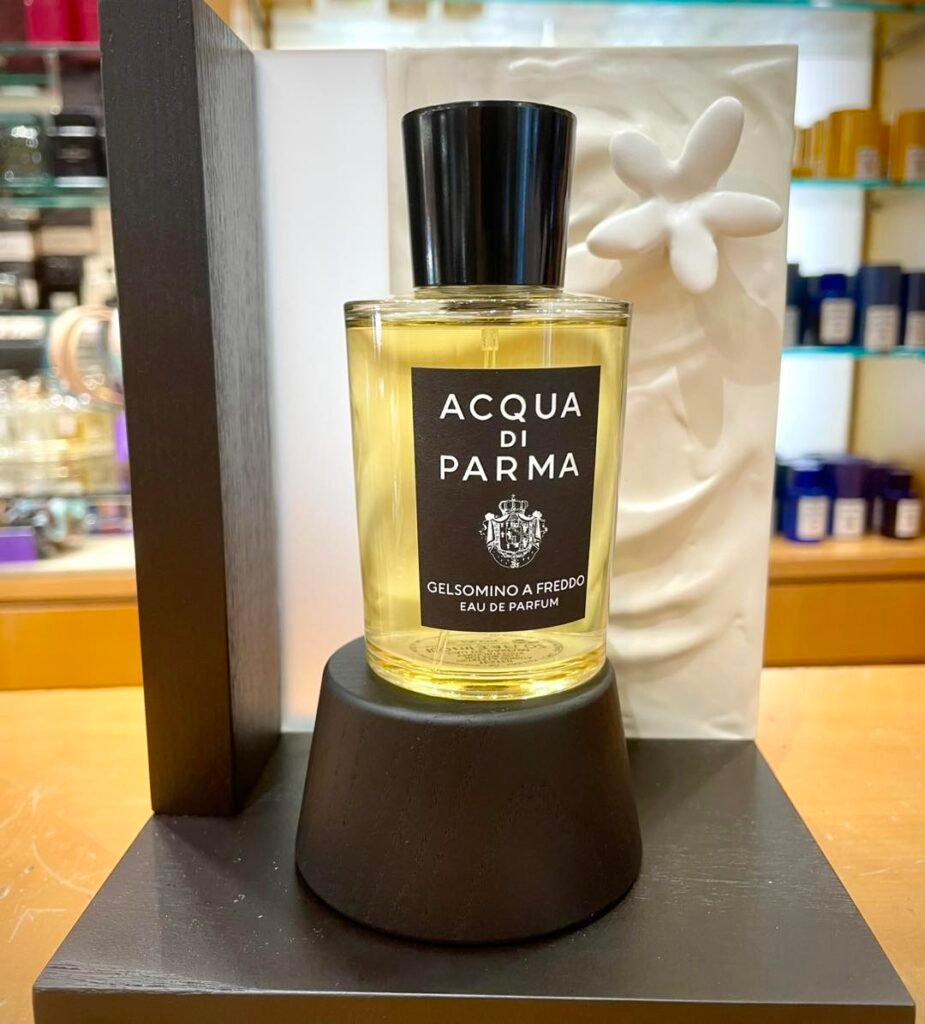 A bottle of Acqua di Parma Gelsomino A Freddo Eau de Parfum displayed on a wooden stand, with a decorative white element in the background.