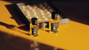 Two bottles of Acqua di Parma perfume on a yellow surface, with a tray of flowers in the background.