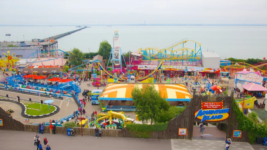 Aerial view of Adventure Island amusement park with various colorful rides, attractions, and a sign indicating it's a free admission fun park, located near the seashore and a long pier extending into the water.