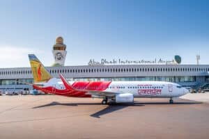 An Air India Express plane on the tarmac at Abu Dhabi International Airport, with the terminal and control tower visible in the background.