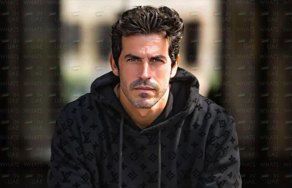 DJ Arodes wearing a black patterned hoodie, looking intently at the camera, with a background that has "What's Hot in UAE" repeated multiple times.