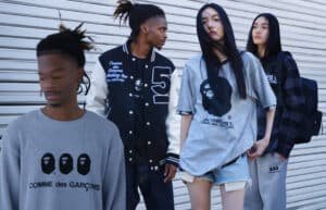 Four people are standing in front of a metal shutter, wearing BAPE clothes featuring "Comme des Garçons" and stylized face designs. The person in the foreground has blurred features and a grey sweater, while others wear a varsity jacket, oversized t-shirts, and casual pants.