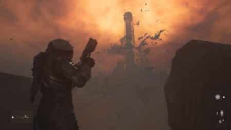 A person wearing a futuristic armored suit holding a large gun, standing in a desolate landscape with a fiery orange sky and debris flying around a distant structure.