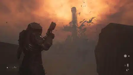 A person wearing a futuristic armored suit holding a large gun, standing in a desolate landscape with a fiery orange sky and debris flying around a distant structure.