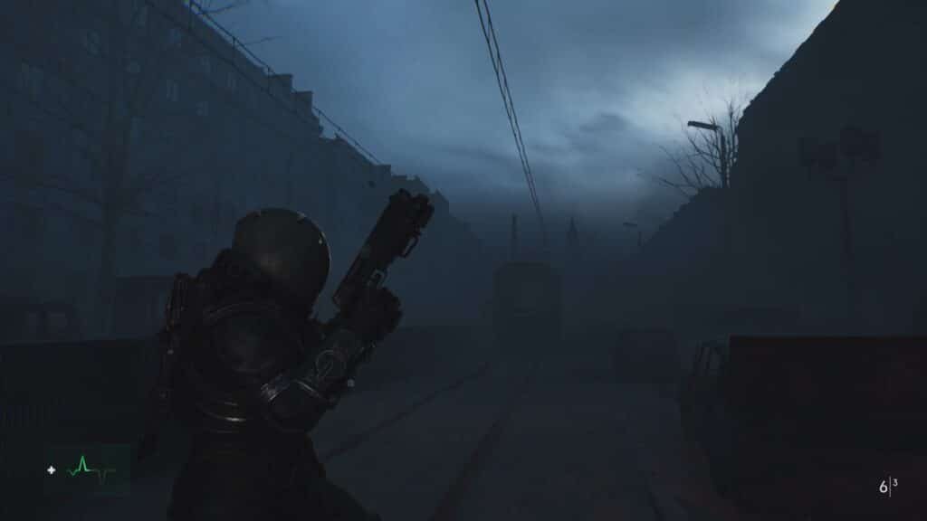 A person in futuristic armor is holding a gun and standing in a dark, foggy urban street, with silhouettes of buildings and trees visible in the background.