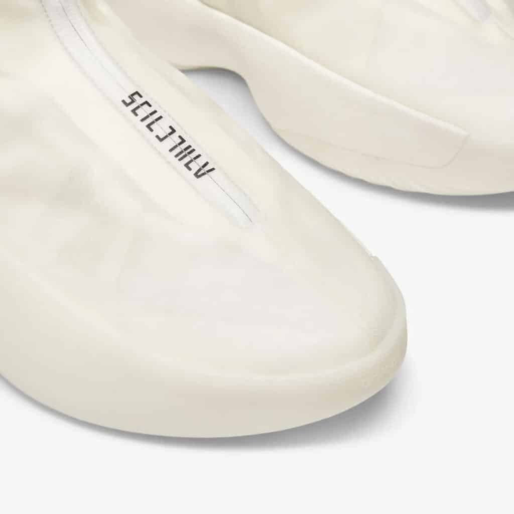 Close-up view of white sneakers with minimalistic design and the word "ATHLETICS" printed along the seam on the upper material.