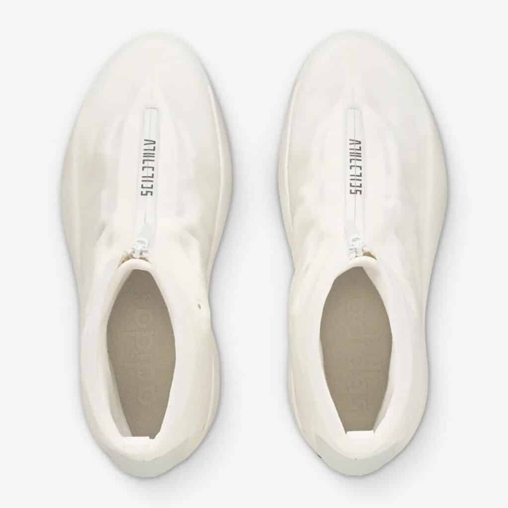 Top view of a pair of white Adidas shoes with closed zippers on the top of each shoe, and the word "ATHLETICS" printed along the zippers.