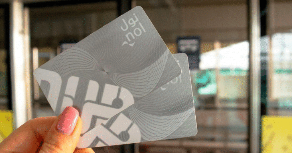 A person holding two silver nol cards, used for transportation payment, in front of a train station entrance.