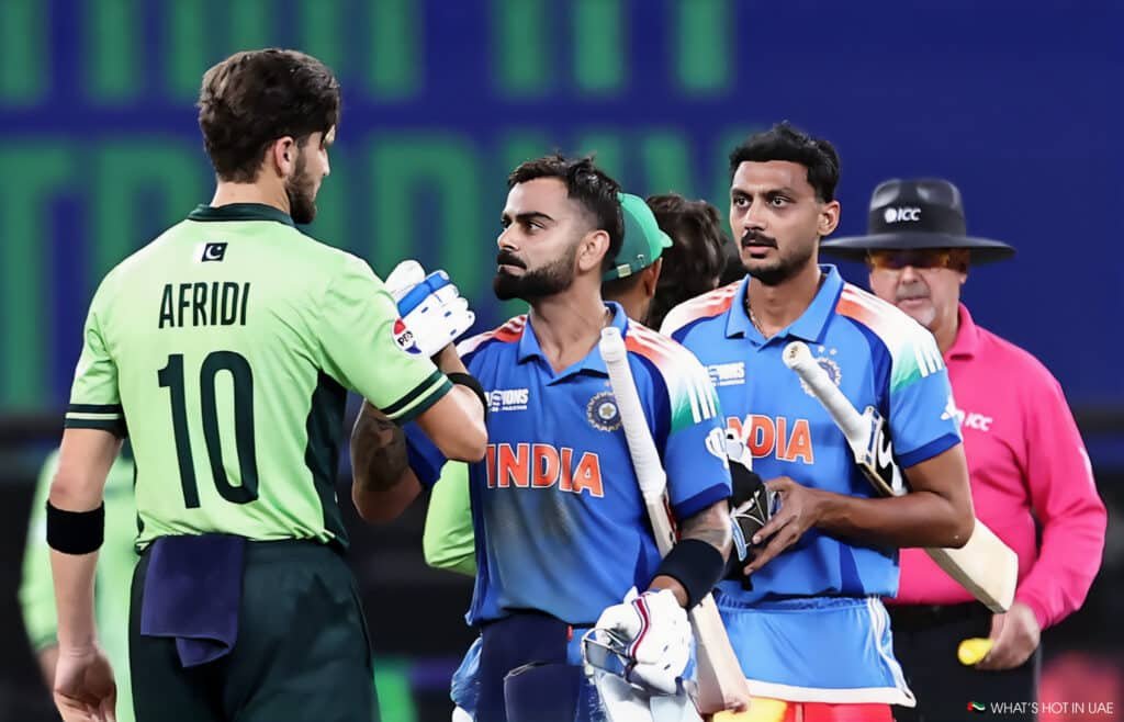 A cricket player in a green jersey labeled "AFRIDI 10" shakes hands with a player in a blue India jersey, with another Indian player and an umpire in the background during a match.