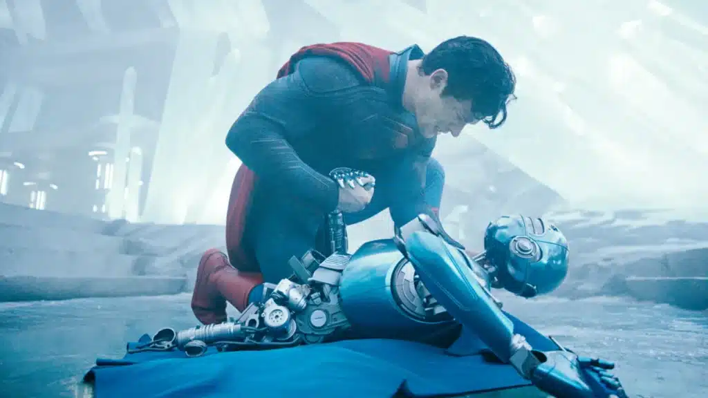 Superman kneels over a blue humanoid robot in a futuristic environment with icy structures.