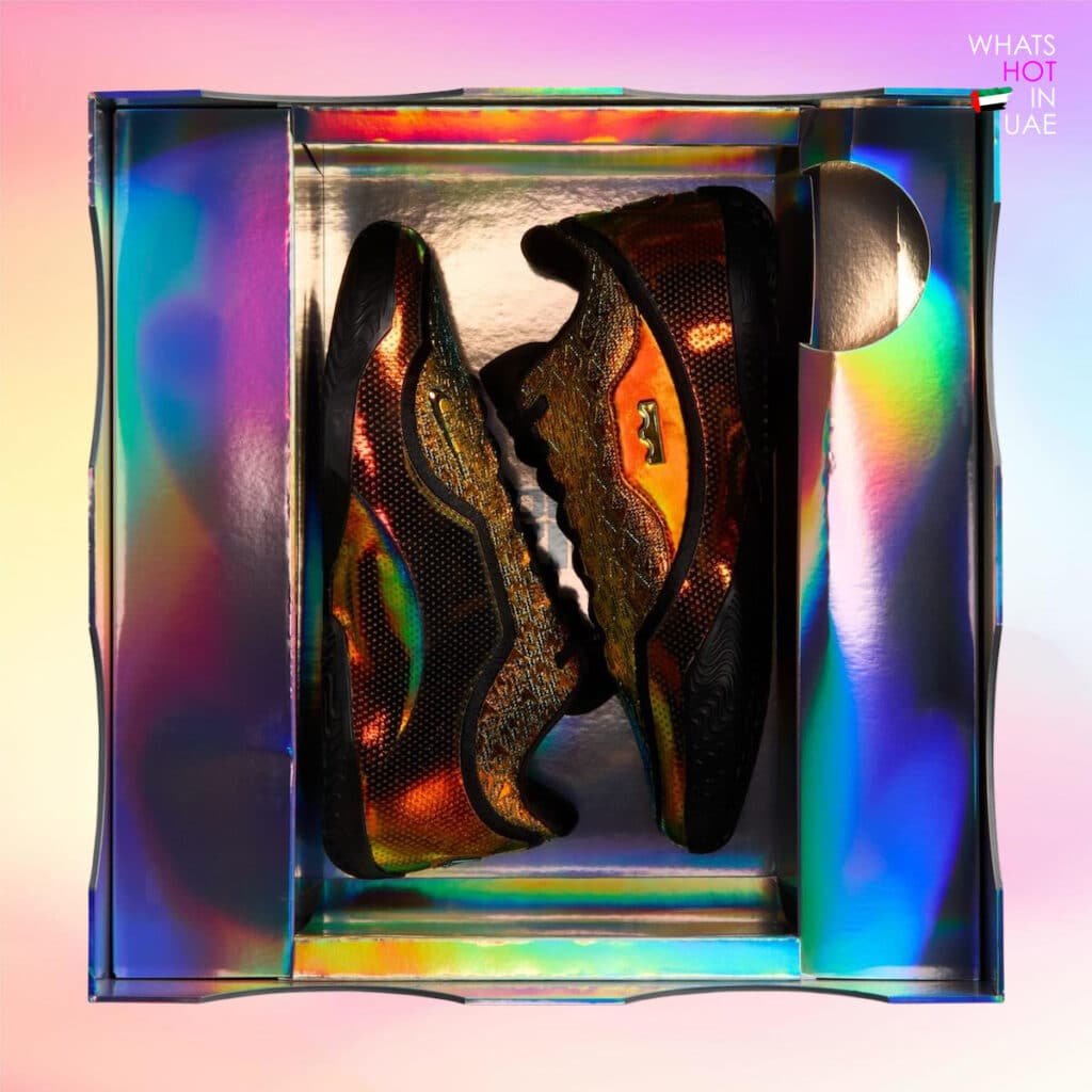 A pair of black and gold textured sneakers displayed in an iridescent, holographic shoe box with a reflective pink and blue interior. Nike LeBron 23 “40K Gold”