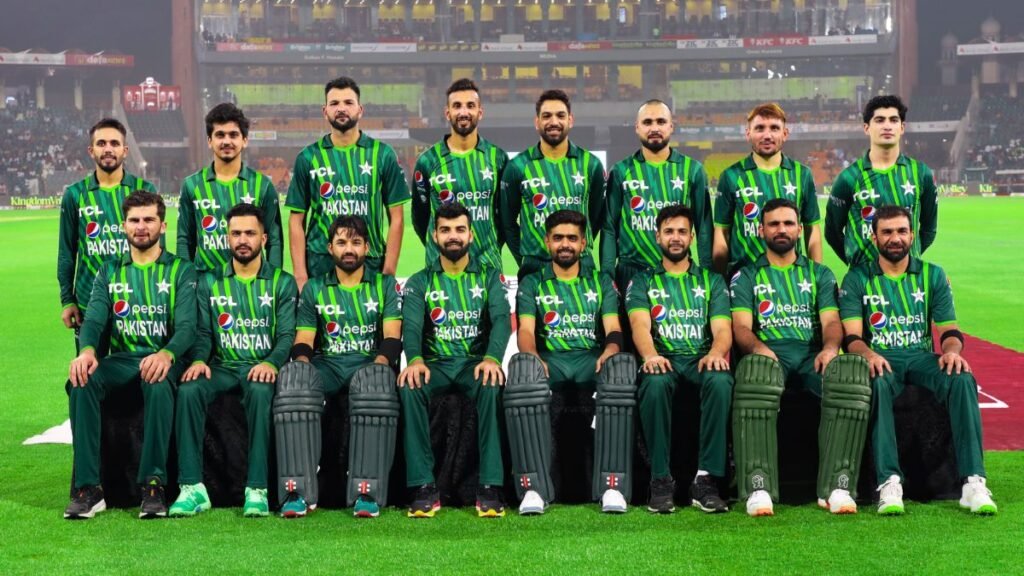 A group of cricketers from the Pakistan national team posing for a team photo in green and black uniforms on a cricket field, with a stadium in the background. Pak vs Afg